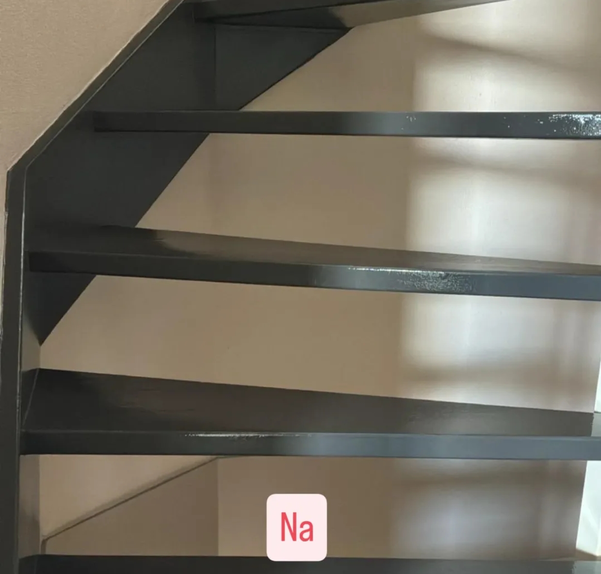 Een afgewerkte trap met donkergrijs gelakte treden en stootborden, met het label Na